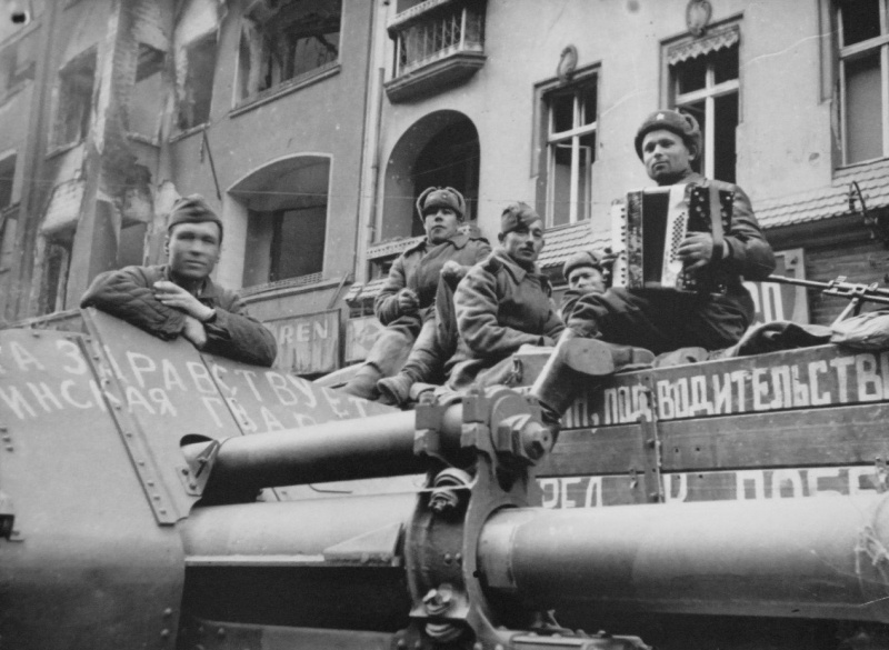 Советские артиллеристы слушают игру на аккордеоне своего товарища на улице Берлина. На переднем плане — 122-мм гаубица М-30. Источник: altyn73.livejournal.com. Май 1945 года. Автор неизвестен 