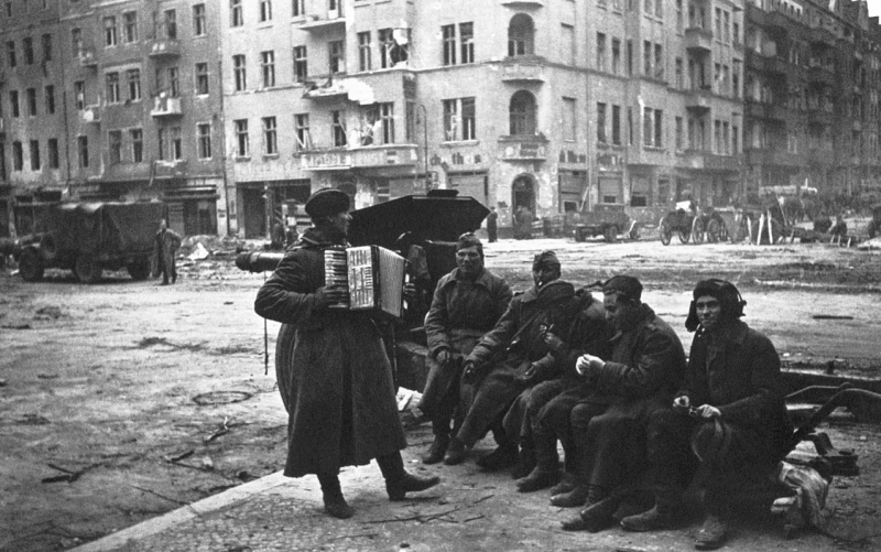 Советские солдаты слушают гармониста, сидя на станине 122-мм гаубицы М-30 на улице Берлина. 1945 год. Автор фото:  Аркадий Шайхет
