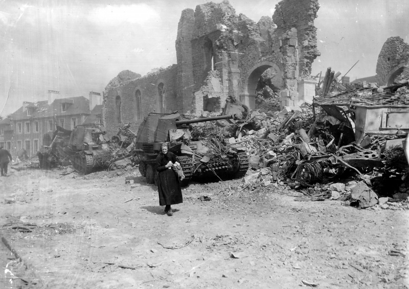 Пожилая женщина идёт мимо разрушенной церкви города Ронсе. У подножия церкви уничтоженная колонна немецкой техники, в том числе две САУ Marder III.