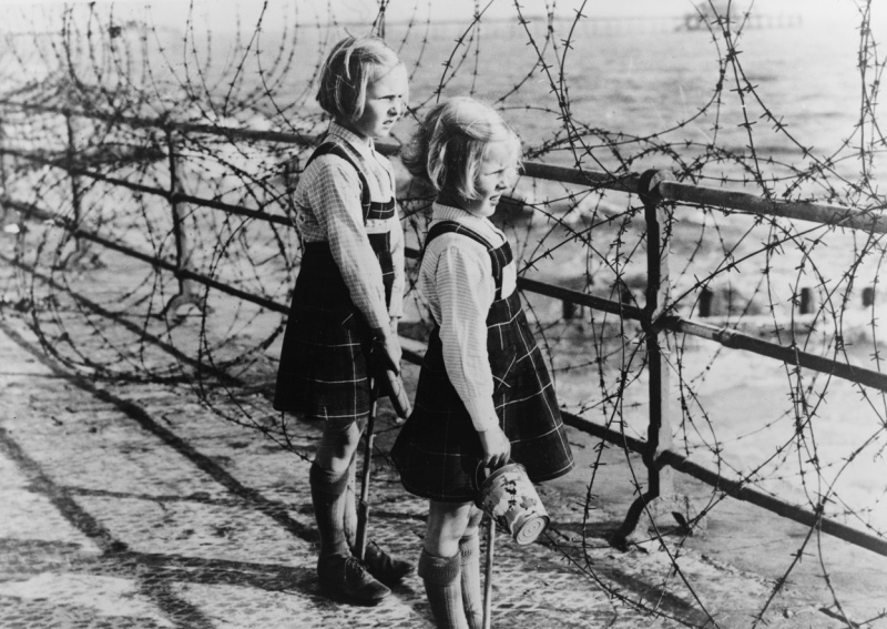 Две девочки смотрят сквозь колючую проволоку береговых укреплений на море и пляж на южном побережье Англии во время битвы за Британию.